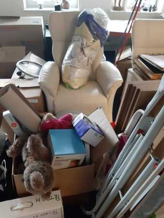 Weißer Sessel in einem chaotischen Raum mit Umzugskartons, Spielzeug und Haushaltswaren.